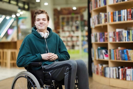 Man in wheelchair with headphones around neck in a library